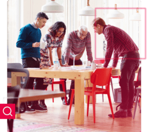 4 pessoas ao redor de uma mesa de trabalho observando um projeto